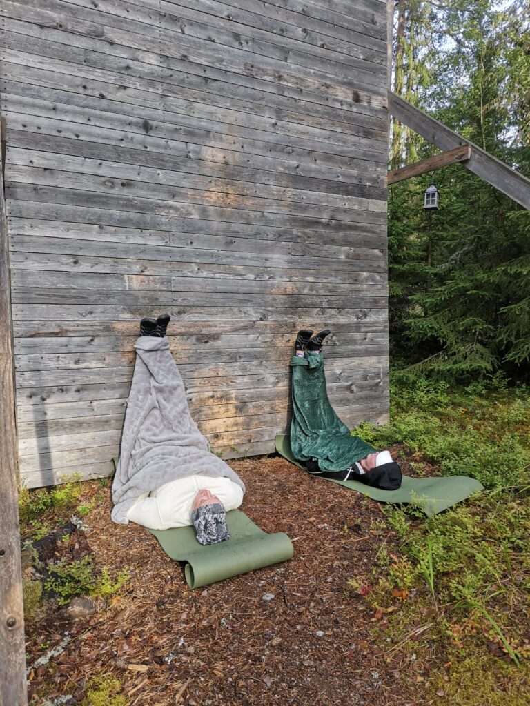 Joskus on parempi vain levätä. Kaksi naista makaa maassa kietoutuneina viltteihin, jalat vasten seinää nostettuna.