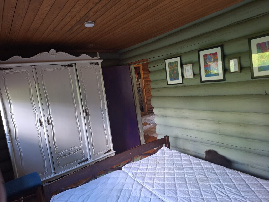 Kuvassa mökkimme vihreä makuuhuone huoneen perältä päin kuvattuna ja siinä näkyy iso valkoinen puinen vaatekaappi sängyn lisäksi.