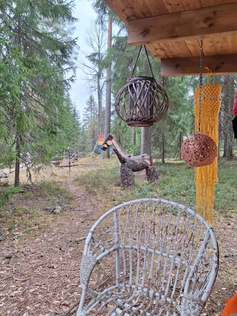 Lammaskahvila - kuvassa näkymä laavulta. Näkyy rakkauden seinä ja huolihevonen eli laudoista ja kanaverkosta rakennettu hevonen, jonka sisällä on käpyjä. Käpyjä voi kerätä kuka vaan omien huoliensa mukaan ja jättää huolensa käpyjen muodossa hevoseen.