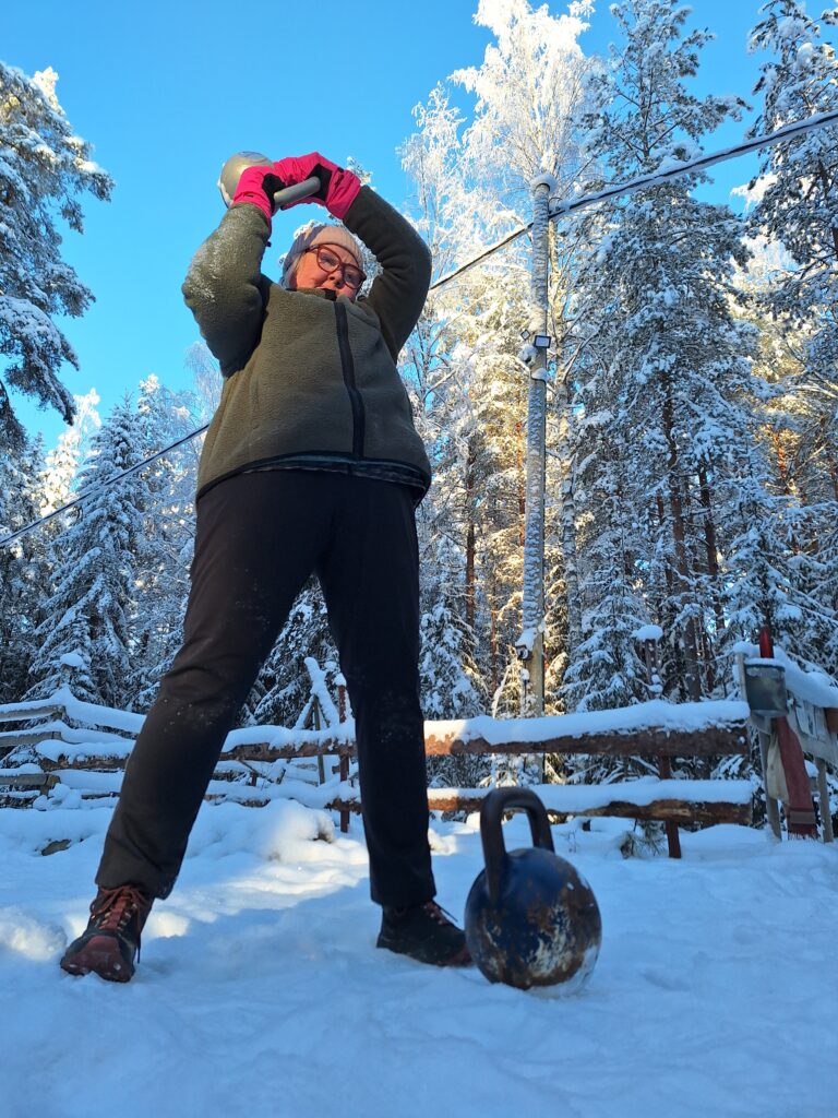 Valon voima - kuvassa keski-ikäinen nainen treenaan kahvakuulalla lumisessa maisemassa, jossa on kaunis sininen valo.